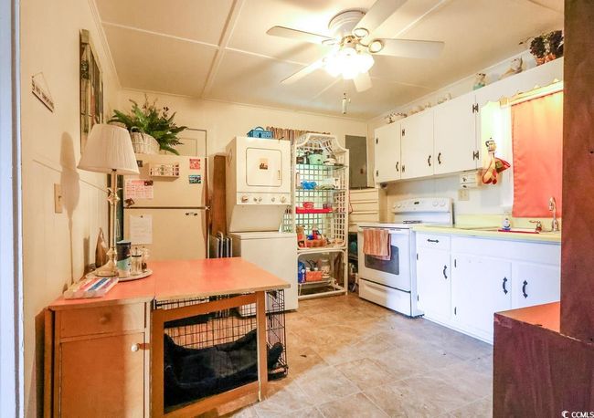 Kitchen with white range with electric stovetop, stacked washer and clothes dryer, ceiling fan, light countertops, and white cabinetry | Image 26