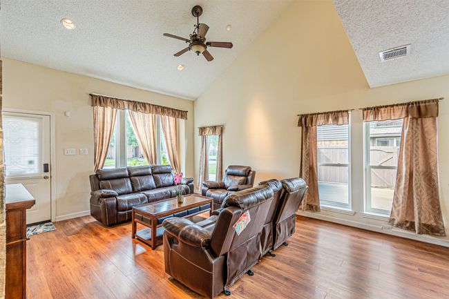 Living room with a textured ceiling, a ceiling fan, high vaulted ceiling, and wood finished floors | Image 7