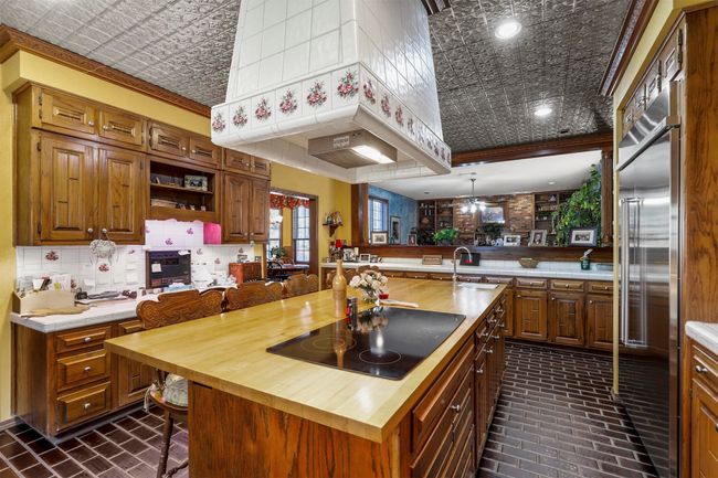 Kitchen featuring black electric cooktop, a kitchen island with sink, built in refrigerator, kitchen peninsula, and wooden counters | Image 17