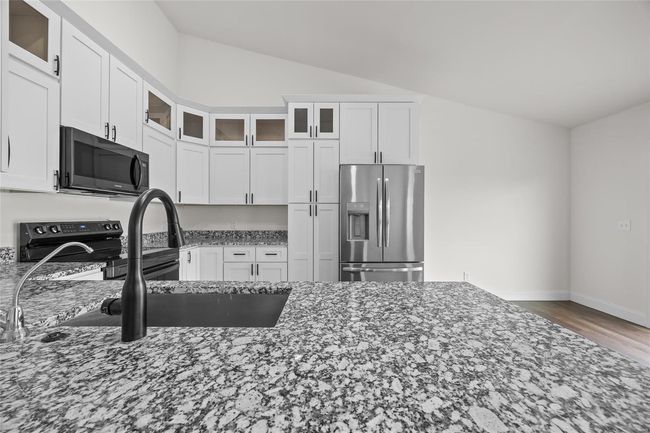 Kitchen featuring white cabinets, electric stove, dark stone counters, stainless steel refrigerator with ice dispenser, and vaulted ceiling | Image 27