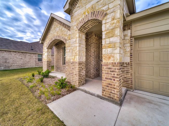 View of exterior entry with brick siding, a garage, a yard, and stone siding | Image 4