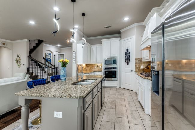 Kitchen featuring appliances with stainless steel finishes, ornamental molding, light stone countertops, white cabinetry, and decorative backsplash | Image 9