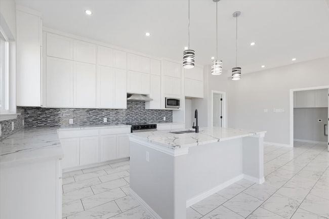 Kitchen with light marble finish flooring, stainless steel microwave, under cabinet range hood, white cabinets, and recessed lighting | Image 13