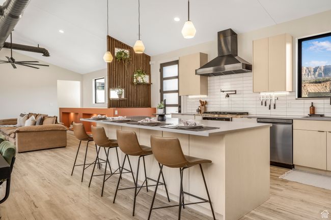 Kitchen featuring light wood-type flooring, wall chimney range hood, a kitchen island, lofted ceiling, and stainless steel appliances | Image 14