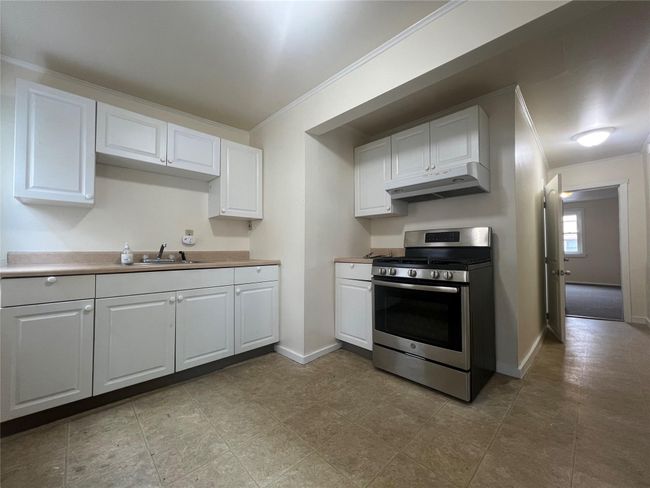 Kitchen featuring gas stove, under cabinet range hood, a sink, white cabinets, and crown molding | Image 4