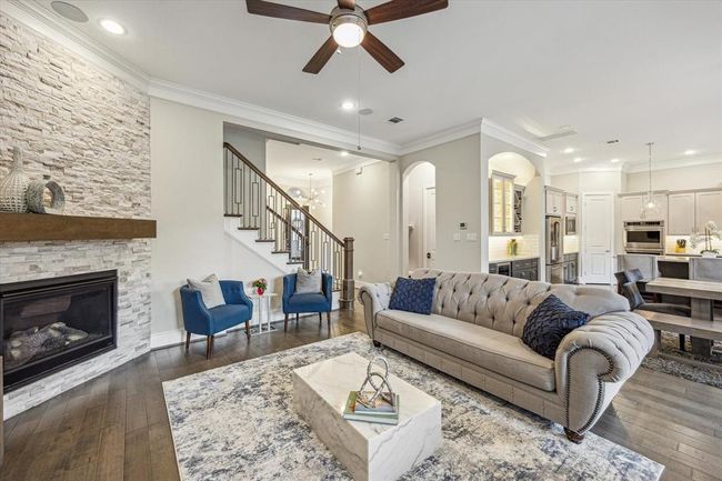 The living area features an elegant stone fireplace, modern ceiling fan, and hardwood floors. The open concept connects seamlessly to your kitchen & dining room. Perfect for entertaining and relaxation. | Image 8