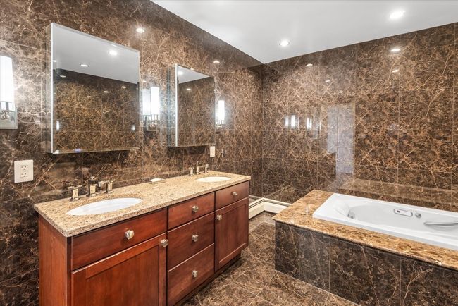 Bathroom with a garden tub, double vanity, a sink, and tile walls | Image 11
