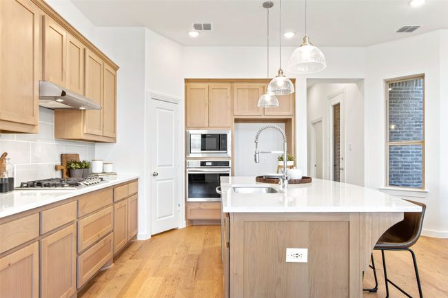 Kitchen featuring appliances with stainless steel finishes, light brown cabinets, light wood-style floors, backsplash, and light countertops | Image 18