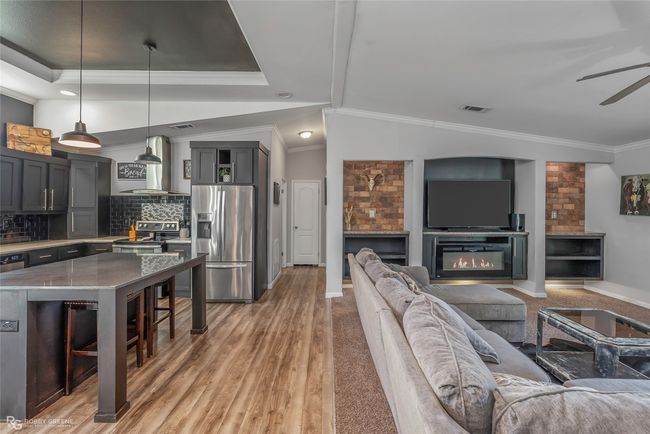 Living area with visible vents, ornamental molding, ceiling fan, a glass covered fireplace, and light wood-type flooring | Image 14