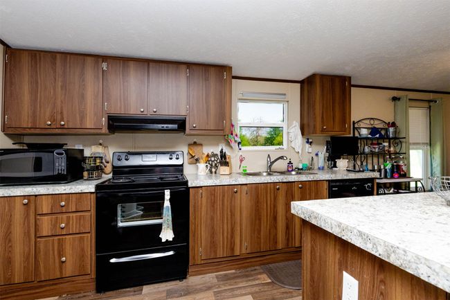 Kitchen featuring brown cabinetry, black appliances, under cabinet range hood, light countertops, and a sink | Image 9