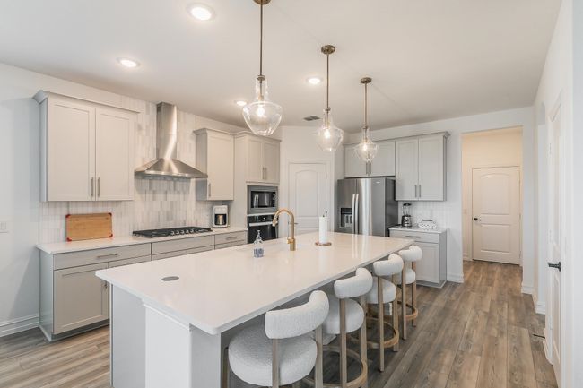 Kitchen featuring backsplash, stainless steel appliances, wall chimney exhaust hood, and an island with sink | Image 11