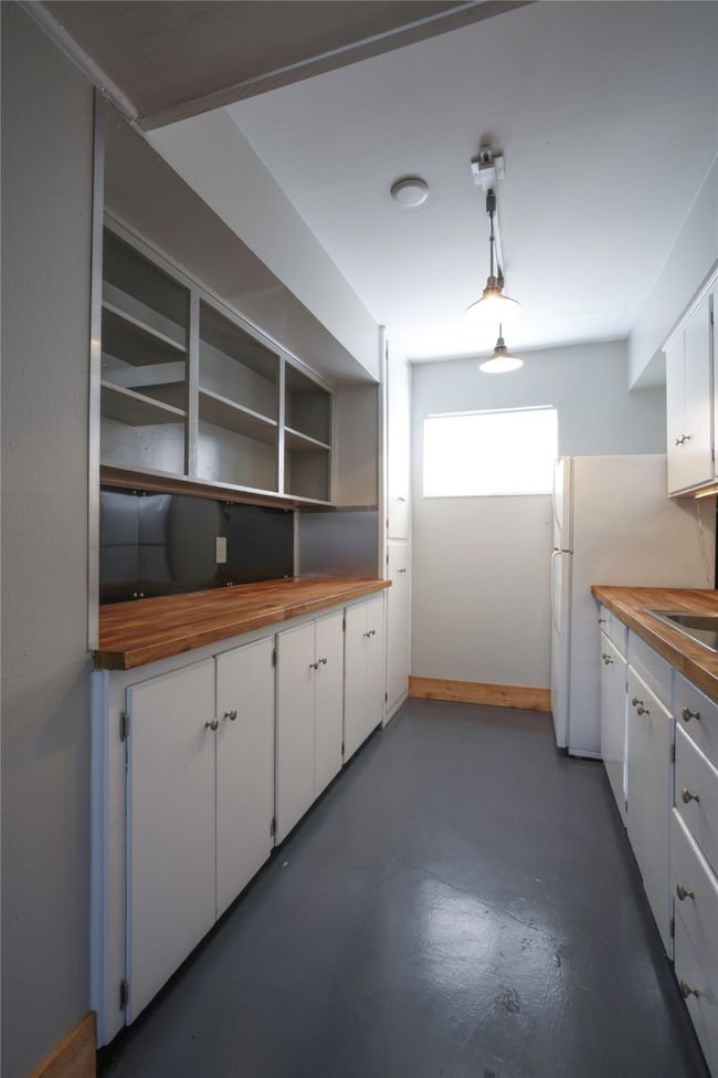 Kitchen featuring butcher block countertops, finished concrete floors, white cabinets, freestanding refrigerator, and pendant lighting | Image 10