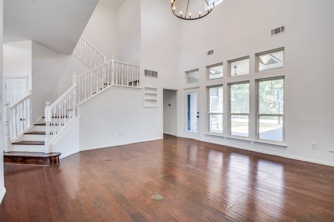Unfurnished living room with stairs, a chandelier, wood finished floors, a towering ceiling, and baseboards | Image 6