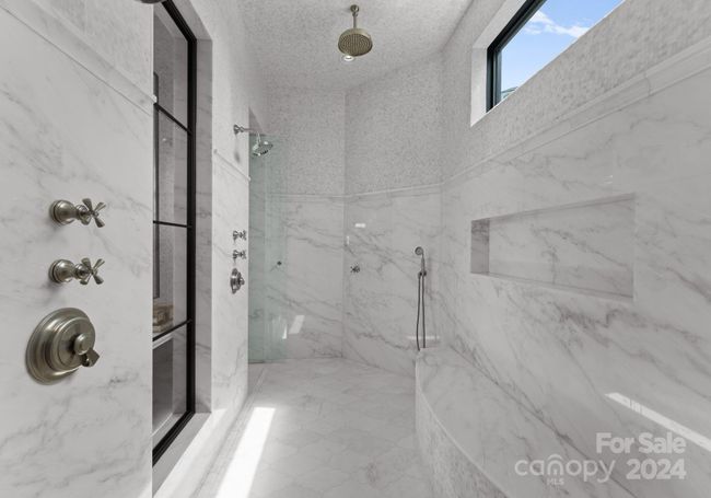 Expansive walk thru shower adorned with marble from the ceiling to the floor. The shower features rain shower heads, body sprayers, and traditional shower heads. | Image 22