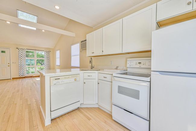Kitchen with white appliances, vaulted ceiling, white cabinets, light wood-style floors, and a peninsula | Image 9
