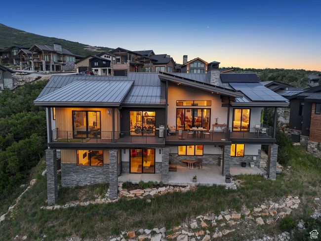 Back of property at dusk featuring a standing seam roof, a patio, stone siding, and a balcony | Image 82