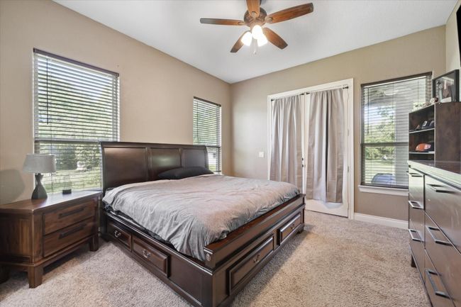 This bedroom features large windows for natural light, and a ceiling fan. It has neutral walls and carpeting, creating a cozy atmosphere. There's access to the outdoors through glass doors. | Image 13