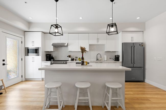 Kitchen featuring a kitchen island, under cabinet range hood, a sink, stainless steel appliances, and a breakfast bar area | Image 5