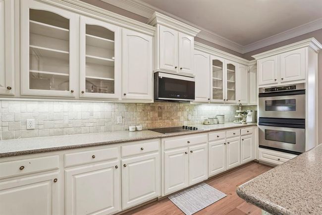 This kitchen features elegant white cabinetry with glass-fronted upper cabinets, a built-in microwave, and double ovens. The neutral backsplash complements the sleek countertops, creating a bright and inviting cooking space. | Image 24