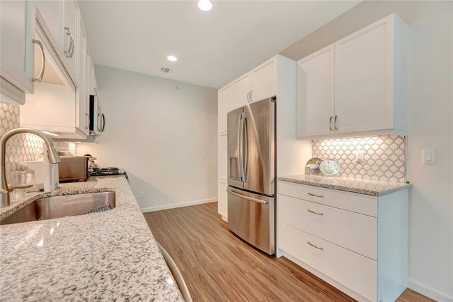 Kitchen featuring stainless steel appliances, light wood finished floors, white cabinetry, tasteful backsplash, and light stone counters | Image 7