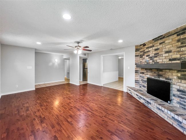 Unfurnished living room featuring wood finished floors, a fireplace, ceiling fan, a textured ceiling, and recessed lighting | Image 8