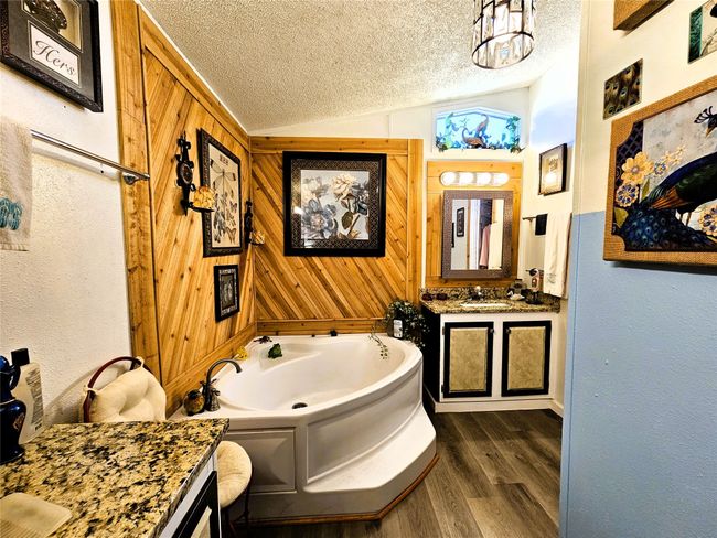 Full bathroom featuring a textured ceiling, wood finished floors, vaulted ceiling, a garden tub, and vanity | Image 11
