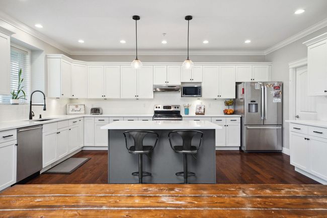 Kitchen with crown molding, a kitchen island, under cabinet range hood, stainless steel appliances, and a sink | Image 11