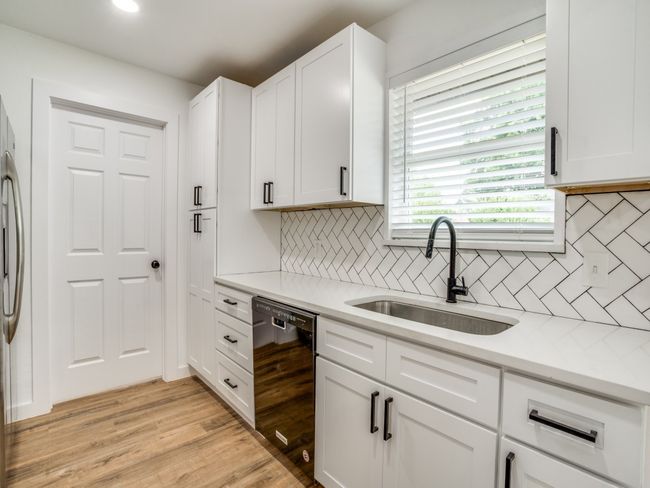 Kitchen with black dishwasher, a sink, white cabinetry, tasteful backsplash, and light countertops | Image 5