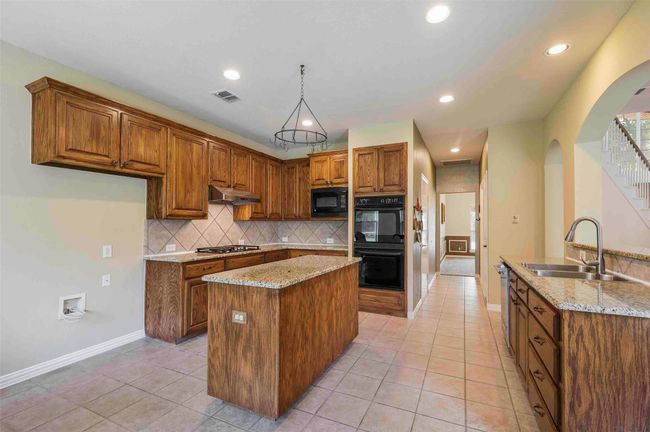 Kitchen with a sink, black appliances, visible vents, a kitchen island, and arched walkways | Image 12