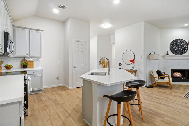 Kitchen with stainless steel microwave, light wood-type flooring, a sink, a kitchen breakfast bar, and baseboards | Image 8
