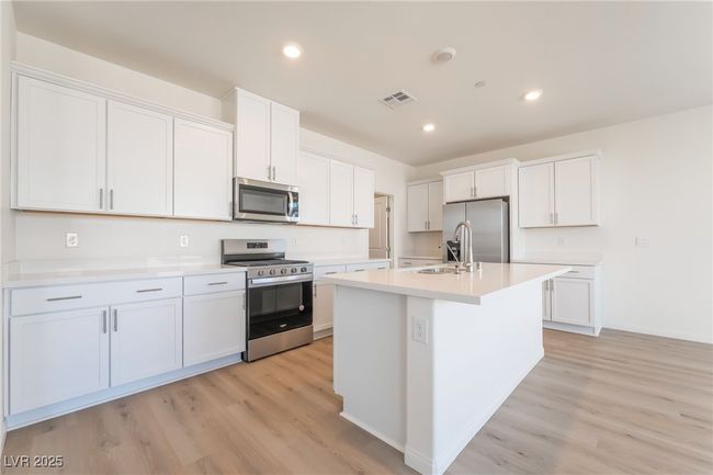 Kitchen featuring stainless steel appliances, light wood finished floors, a center island with sink, white cabinetry, and recessed lighting | Image 11