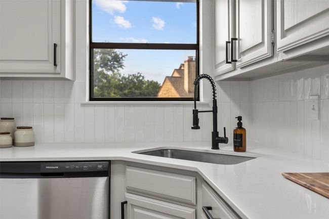 Kitchen with stainless steel dishwasher, decorative backsplash, light countertops, and white cabinetry | Image 21