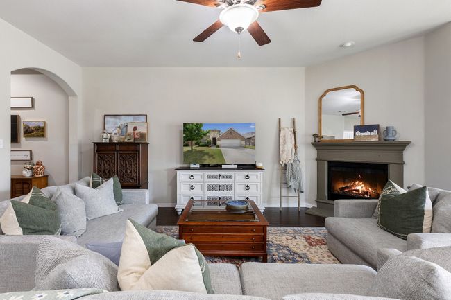 Living room with arched walkways, dark wood finished floors, baseboards, ceiling fan, and a lit fireplace | Image 7