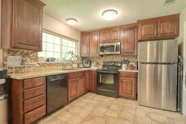 Kitchen featuring black appliances, backsplash, a textured ceiling, light stone counters, and brown cabinets | Image 17