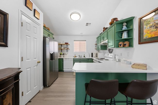 Kitchen with a peninsula, green cabinets, open shelves, and white appliances | Image 9