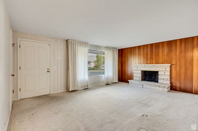 Unfurnished living room featuring wooden walls, a stone fireplace, visible vents, and carpet | Image 4