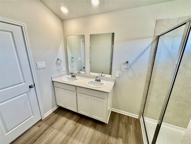 Full bath featuring wood finished floors, a shower stall, double vanity, and a textured wall | Image 4