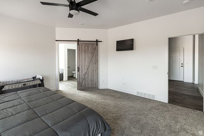 Bedroom with carpet flooring, visible vents, ceiling fan, a barn door, and baseboards | Image 10