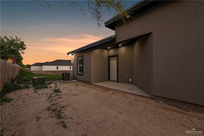 Back of house at dusk with a patio area, central air condition unit, fence, and stucco siding | Image 4