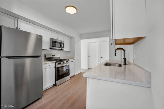 Kitchen with a sink, white cabinets, light wood-type flooring, and stainless steel appliances | Image 10