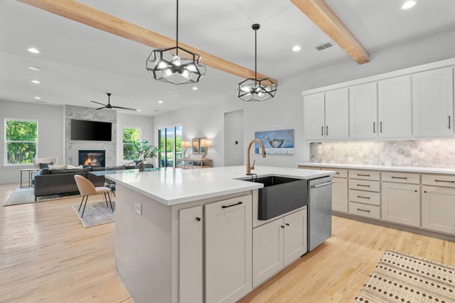 Kitchen featuring stainless steel dishwasher, beam ceiling, backsplash, a large fireplace, and an island with sink | Image 15