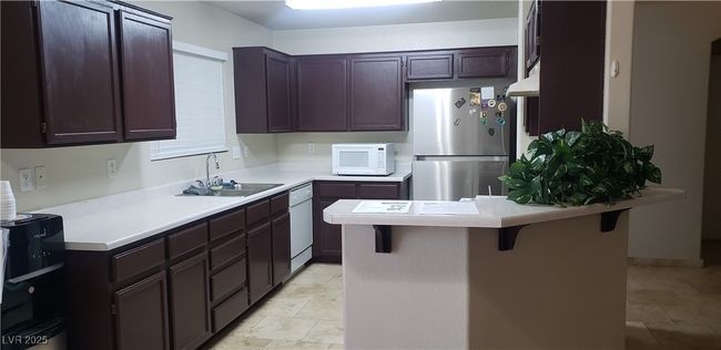 Kitchen featuring white appliances, a breakfast bar area, a sink, light countertops, and a peninsula | Image 17