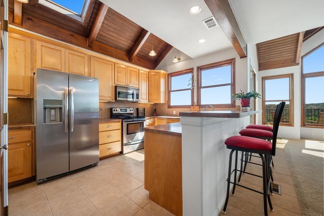 Kitchen featuring stainless steel appliances, wood ceiling, a breakfast bar area, maple cabinetry, and a skylight. | Image 13