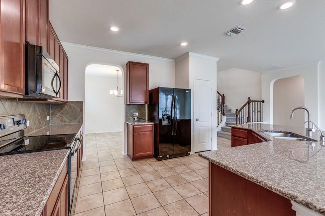 Kitchen with stainless steel electric range oven, black refrigerator with ice dispenser, visible vents, arched walkways, and a sink | Image 9