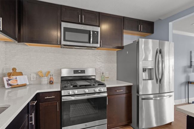 Kitchen featuring light stone countertops, stainless steel appliances, dark brown cabinetry, crown molding, and backsplash | Image 13