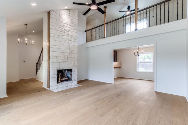 Unfurnished living room with a chandelier, a ceiling fan, stairway, a high ceiling, and a stone fireplace | Image 6