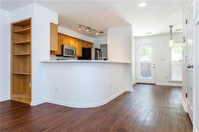 Kitchen featuring stainless steel appliances, brown cabinetry, dark wood-style floors, light countertops, and a peninsula | Image 4