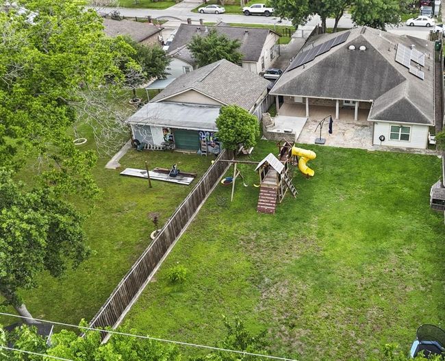 This aerial view showcases a spacious backyard with a well-maintained lawn, complete with a children's play structure and ample room for outdoor activities. The property is bordered by a wooden fence for privacy and sits within a residential neighborhood with nearby houses. | Image 10