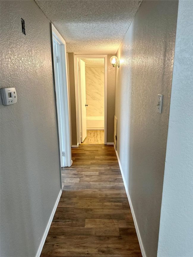 Corridor featuring a textured ceiling, dark wood-style floors, baseboards, and a textured wall | Image 5