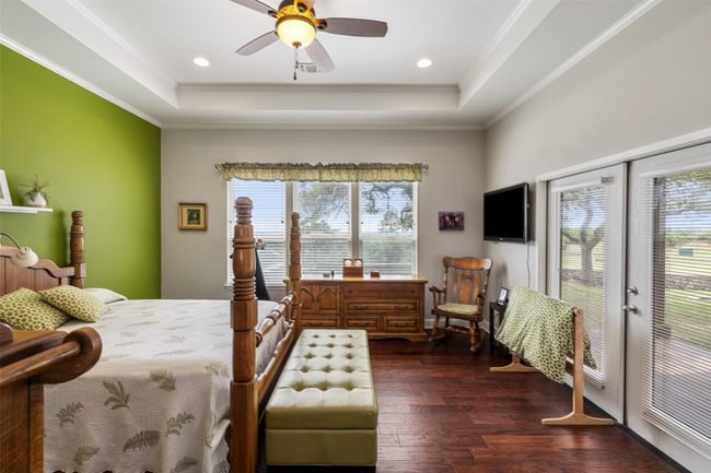 Bedroom with dark wood-type flooring, a raised ceiling, crown molding, and multiple windows | Image 37